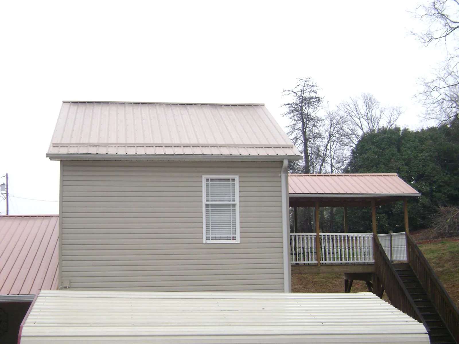 Tan metal roofs on a two story addition and attached porch, from a Roof Replacement job in Arlington